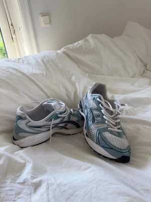 Asics gel kayano 14 - Säljer ett par snygga sneakers i vitt och ljusblått med silvriga detaljer. Skorna heter asics gel kayano 14 och är i storlek 41,5