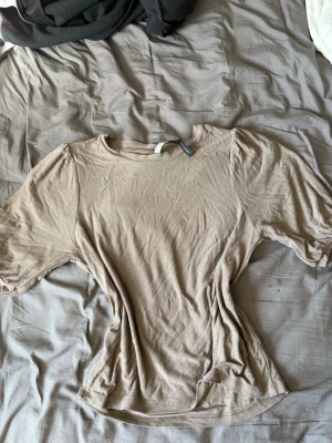 Beige t-shirt från The Black Label - Snygg beige t-shirt från The Black Label i mjuk bomull. Modellen har rund halsringning och korta ärmar. Perfekt basplagg att matcha med allt. Enkel och stilren design som passar till många olika looks.
