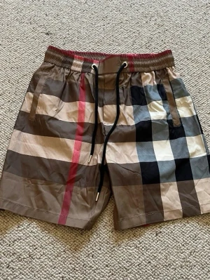 Burberry shorts - Ett par befor beige burberry bad shorts med rutig design. De är i storlek S och i helt nytt skick. Pris kan diskuteras och skriv om du har några frågor. 