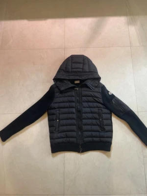 moncler cardigan  - Säljer en svart cardigan från Moncler med stickade ärmar och vadderad kropp. Jackan har en stor huva, dragkedja framtill och två sidofickor med dragkedja. Jättefin på vintern och även i hösten Nypris 3500kr mitt pris ENDAST 2100kr !