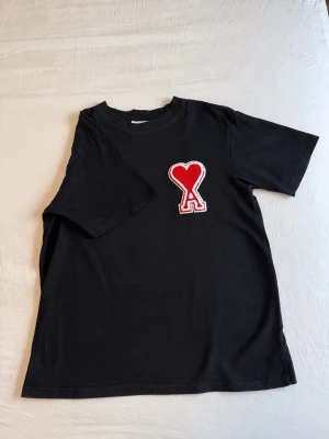 Svart t-shirt med rött hjärta - Svart t-shirt med ett stort rött hjärta och bokstaven A broderat på bröstet. Klassisk rund hals och korta ärmar. Perfekt för en avslappnad och trendig stil.
