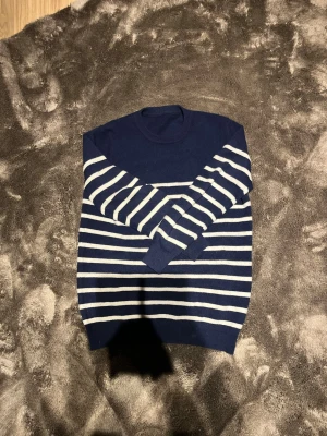 Marinblå randig stickad tröja - Snygg marinblå stickad tröja med vita horisontella ränder. Tröjan har rund halsringning och långa ärmar. Perfekt för dig som gillar klassisk och stilren design. Materialet ser mjukt och bekvämt ut, passar bra till jeans. Nypris 899