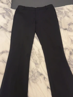 svarta kostymbyxor - Snygga mörkgrå kostymbyxor med utsvängda ben och hällor för skärp. Byxorna har två fuskfickor bak och klassisk midja. Perfekta för en stilren look och passar till många olika outfits.