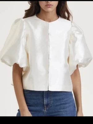 Vit blus med puffärmar - Säljer en stilren vit blus med stora puffärmar och rund halsringning. Blusen har en rak passform och är tillverkad i ett glansigt, strukturerat material som ger en lyxig känsla. Perfekt för dig som vill sticka ut med en trendig och elegant look.