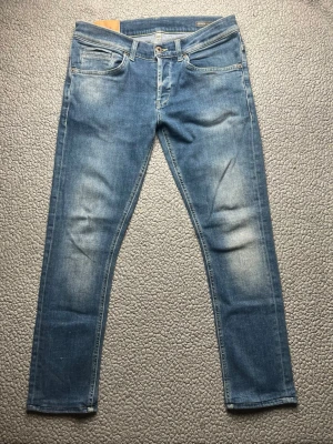 Blå slim fit jeans från Dondup George - Snygga blå slim fit jeans från  Dondup George med klassisk femficksdesign och ljusa slitningar på låren. Jeansen har gul kontrastsöm och normalhög midja. Perfekta för en avslappnad och trendig look.