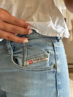 Ljusblå bootcut jeans Diesel - Säljer ett par ljusblå bootcut jeans från Diesel med klassisk femficksdesign och diskret logga på myntfickan. Jeansen har låg midja och är tillverkade i mjuk denim som ger en snygg passform. De är lite slitna vid foten.