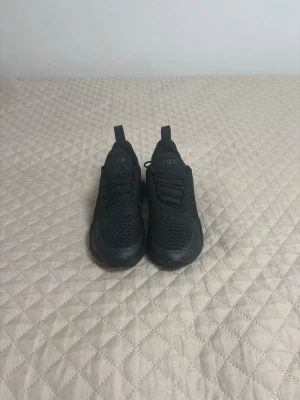 Svarta Nike Air Max 270 sneakers - Säljer ett par helsvarta Nike Air Max 270 sneakers med mesh-ovandel och synlig Air-enhet i hälen. Skorna har en sportig look med diskreta detaljer och snörning. Perfekta för dig som gillar stilrena och bekväma sneakers.