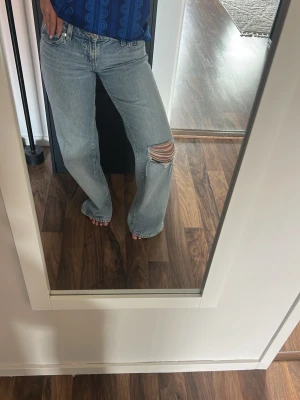 Low waist baggy jeans  - Säljer ett par ljusblå jeans med rak passform och ett stort slitet hål på ena knät. Säljer då det blev fel storlek