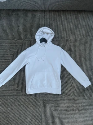 Vit basic hoodie från Pier one  - En stilren vit hoodie med huva och dragsnören. Klassisk känguruficka framtill och ribbade muddar vid ärmslut och nederkant. Perfekt för en clean och avslappnad look. Materialet ser ut att vara mjukt och bekvämt, troligen bomullsblandning.