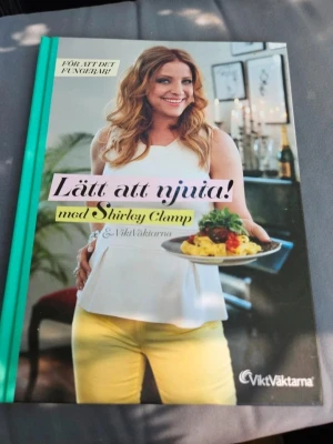 Lätt att njuta! med Shirley Clamp - En inspirerande kokbok med färgglatt omslag och hårda pärmar. Boken innehåller recept och tips från Shirley Clamp och ViktVäktarna, med fokus på hälsosam och god mat. Perfekt för dig som vill laga enkla och smakrika rätter.