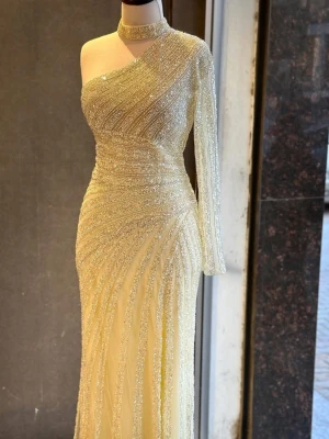Glittrig långklänning med oneshoulder stl 32/34 - Elegant långklänning i ljusgul nyans med glittriga ränder. Klänningen har oneshoulder-design med en lång ärm och hög krage, samt en slits framtill. Perfekt för speciella tillfällen där du vill sticka ut. Den passar stl 32/34. Jag har Byst:82 cm Midja: 72 cm Höfter: 97cm. Det finns en liten fläck på klänningen, men den syns inte eftersom den sitter på insidan. Jag har till och med lämnat in den på kemtvätt, men fläcken gick inte bort. Klänningen är dock ren. Den har bara använts en gång.