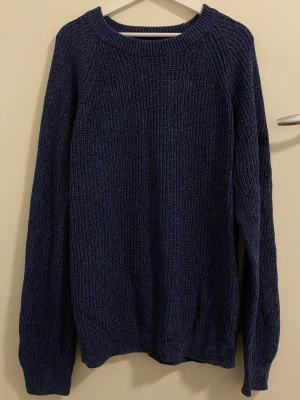 Mörkblå stickad tröja - En enkel och stilren mörkblå stickad tröja med rund halsringning och långa ärmar. Tröjan har en grovstickad struktur och ribbade muddar vid ärmslut och nederkant. Perfekt för kyliga dagar och lätt att matcha med olika outfits.