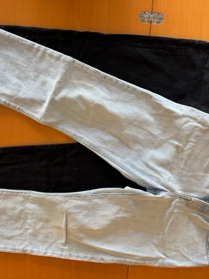 2st Levis 501 raka jeans med knappar - Säljer 2 par Levis 501 jeans med raka ben och knappgylf i svart och ljusblå. Storlek S (w28/29 l30).  Klassisk femficksmodell i denim med silverfärgade nitar och bälteshällor. Perfekta för en avslappnad och trendig look. Materialet är bomullsdenim.
