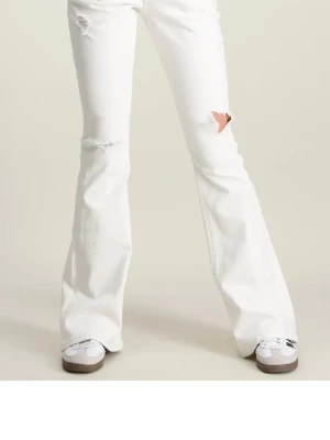 Vita utsvängda jeans med slitningar - Säljer ett par vita jeans med utsvängda ben och snygga slitningar på låren och knäna. Perfekta för dig som vill ha en trendig och avslappnad look. Jeansen har normal passform och är tillverkade i bomull. Storlek M i 14+ vilket är som S.