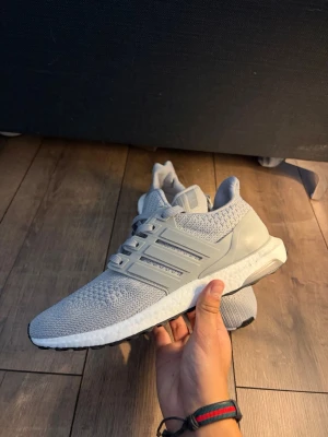 Adidas ultraboost  - Snygga grå Adidas Ultraboost sneakers med stickad ovandel och vita Boost-sulor. Skorna har klassiska tre ränder på sidan, grå snörning och svart yttersula. Perfekta för dig som gillar stilrena och bekväma sneakers med modern design. Passar även 42