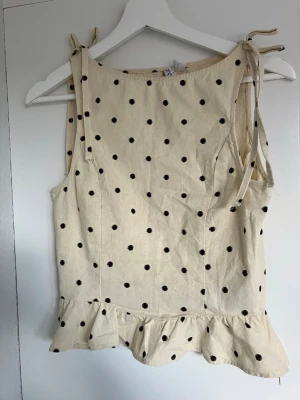 Beige prickig topp med volang - Söt beige topp med svarta prickar, knytband på axlarna och volang längst ner. I storlek Xs från hm