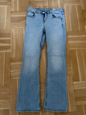 Ljusblå bootcut jeans MIRA W28 L32 - Säljer ett par ljusblå bootcut jeans i modellen MIRA med klassisk femficksdesign och normalhög midja. Jeansen har en snygg tvättad look och raka ben som går ut lite nedtill. Perfekta för en avslappnad och trendig stil.