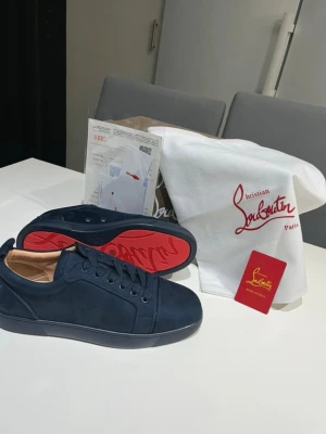 Christian Louboutin marinblåa skor  - Snygga mörkblå sneakers från Christian Louboutin i mocka med klassisk röd sula. Lågt skaft och ton-i-ton snörning ger en clean look. Insidan är beige och skon har diskreta sömmar för en stilren vibe! Kom gärna med bud 