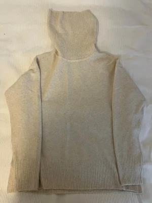 Beige polotröja från Vero Moda - Mysig beige stickad polotröja från Vero Moda. Tröjan har ribbade muddar vid ärmslut och nederkant samt en hög, bred polokrage. Perfekt för lager på lager och enkel att matcha till olika outfits.