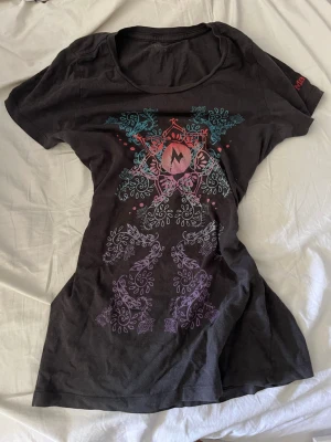 Svart t-shirt med färgglatt mönster - Cool svart t-shirt med färgglatt mandalainspirerat tryck i turkos, rosa och lila på framsidan. T-shirten har rund halsringning och korta ärmar. Perfekt för dig som vill sticka ut med en unik design. Materialet känns mjukt och skönt mot huden.