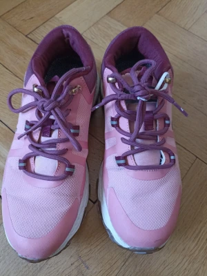 Rosa och lila sneakers med grov sula - Snygga sneakers i rosa och lila med grov brunvit sula och matchande lila snören. Ovandelen är i mesh och syntetmaterial för bra andningsförmåga. Skorna har detaljer i guld vid snörningen och en sportig look som sticker ut.