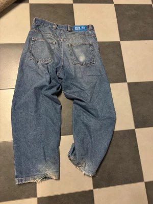 Baggy jeans från Big Boy blå denim - Säljer ett par blå baggy jeans från Big Boy med klassisk femficksdesign och bred passform. Jeansen har slitna detaljer vid bensluten och en tydlig blå label bak i midjan. Perfekta för en avslappnad streetwear-look.