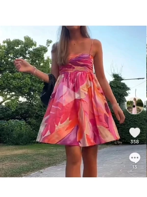 Färgglad kort sommarklänning - Superfin kort klänning med tunna axelband och färgstarkt blommigt mönster i rosa, orange, lila och vitt. Klänningen har en lätt utsvängd kjol och smockad överdel, perfekt för varma dagar. Den har en liten fläck som visas på bild 3, vet ej om den går bort o tvätten🩷🩷