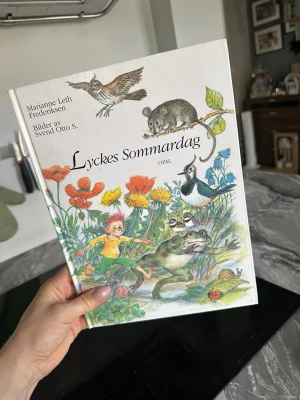 Lyckes Sommardag - bilderbok - En charmig bilderbok med titeln 'Lyckes Sommardag' av Marianne Leth Frederiksen och illustrationer av Svend Otto S. Omslaget är vitt med färgglada teckningar av djur, blommor och en liten pojke. Boken är inbunden och tryckt på papper, perfekt för dig som gillar fantasifulla berättelser och vackra illustrationer.