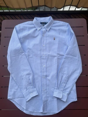 Randig skjorta - äljer denna feta skjorta, märke polo Ralph Lauren. Denna är i betydligt billigare än dem andra jag har på min profil för att denna är INTE äkta. Annars riktigt fin ljusblå randig skjorta som funkade riktigt bra under sommaren. Skulle säga att det är den stor M i storlek. Pris går ej att diskutera på detta plagg. Skickas inom 24h.