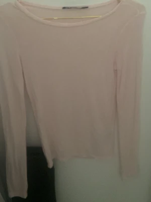 Ljusrosa långärmad topp - Säljer en enkel och stilren ljusrosa långärmad topp med rund hals. Toppen är tunn och har en mjuk känsla, perfekt att styla lager på lager eller bära som den är. Passar till många olika looks och är ett måste i basgarderoben.