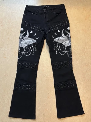 Svarta Gothicana jeans - Svarta Gothicana jeans med snörning och mal-print på höfterna.