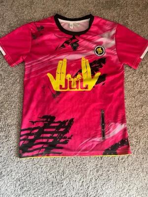 TOTO&NINETTA TRÖJA - Säljer en rosa JUL t-shirt med coola gula tryck fram och bak, bland annat händer, alien och text. T-shirten har svart krage och detaljer i svart och vitt. Perfekt för dig som gillar unika plagg och streetwear vibes.