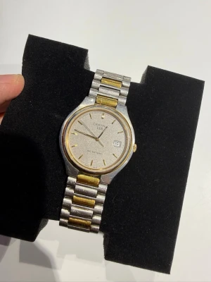 Certina DS herrklocka i silver och guld - Säljer en Certina DS Quartz i tvåtonsutförande (stål/guld). Klockan har datumvisning och originalarmband med Certina-spänne.  Skick: Bruksskick med repor och normalt slitage efter användning. Klockan fungerar, men går ibland långsamt, vilket innebär att den troligen behöver service eller ett nytt urverk/batterikontroll. Den klarar inte trycktest, så den är inte vattentät och bör inte användas vid dusch eller bad.  Säljs därför i befintligt skick och passar bra. 