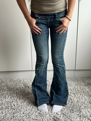 Blå bootcut jeans med låg midja - 33cm rakt över midjan, 78cm innerbenslängd💖 Mittknapp saknas men den har unik midja med knappar på sidan!