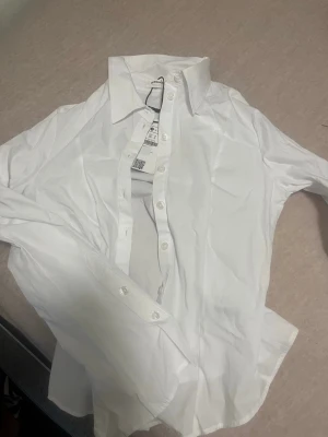 Vit klassisk skjorta från Bershka - Säljer en vit klassisk skjorta från Bershka i storlek S. Skjortan har lång ärm, knappar framtill och en tidlös krage. 
