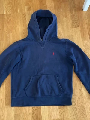 Mörkblå Ralph lauren hoodie - Mörkblå hoodie med huva och magficka. Perfekt för en avslappnad och stilren look. Skick 8/10 mitt pris 349kr kom privat vid intresse storlek 14-16 men passar även upp mot xs