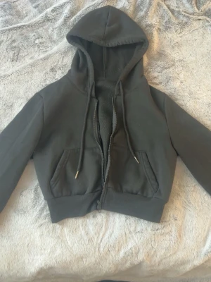 Svart croppad hoodie med dragkedja - Säljer en svart croppad hoodie med dragkedja framtill och två fickor.