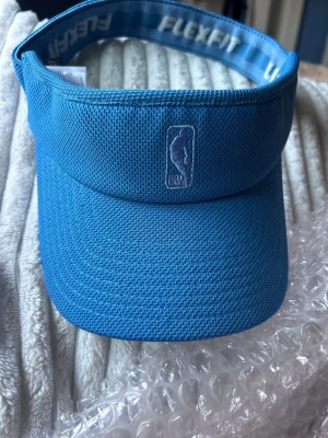 Blå NBA Flexfit keps solskärm  - Snygg blå solskärm från NBA med Flexfit-band och broderad NBA-logga framtill. Tillverkad i ett ventilerande meshmaterial som passar perfekt för sportiga dagar eller när du vill ha en avslappnad stil.