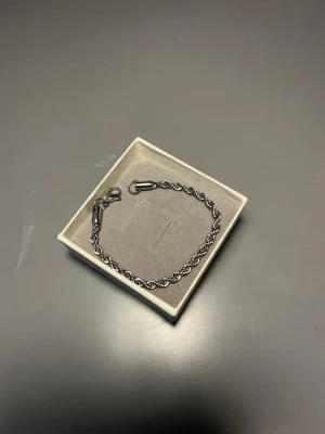 Flätat silverfärgat armband - Snyggt armband i silverfärgad metall med flätad design. Armbandet har en enkel karbinhake och passar perfekt för dig som gillar stilrena accessoarer. Längden är cirka 20 cm. Perfekt att bära ensam eller tillsammans med andra smycken.