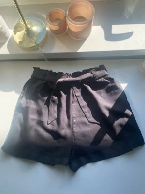 Svarta shorts med knytband - Snygga svarta shorts med hög midja och knytband i midjan. De har en lös passform och är perfekta för varma dagar. Materialet känns mjukt och lätt, vilket gör dem bekväma att bära hela dagen.