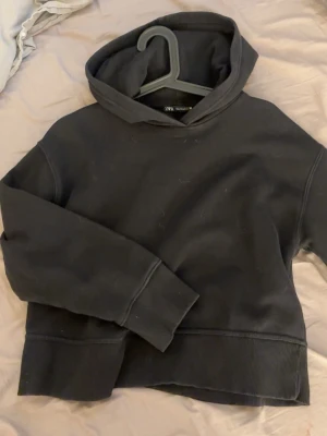 Svart hoodie från Zara - En enkel och stilren svart hoodie från Zara med huva och breda muddar vid ärmslut och nederkant. Hoodien har en avslappnad passform och är tillverkad i mjukt sweatshirtmaterial. Perfekt för en chill och casual look.