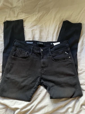 Svarta slim fit jeans från Replay - Säljer ett par svarta slim fit jeans från Replay med klassisk femficksdesign och diskret logga på myntfickan. Jeansen har normal midja och smal passform, perfekta till vardagslooken. Materialet är mjukt och stretchigt för extra komfort.