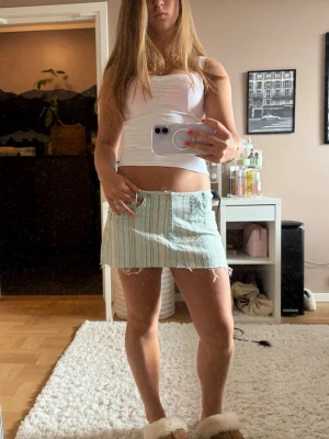 Ljusgrön randig kortkjol - Säljer en ljusgrön kortkjol med tunna vita ränder. Kjolen har råa kanter nertill för en avslappnad look och är tillverkad i ett lätt tyg, perfekt för varmare dagar. Passformen är normal och kjolen har en enkel, stilren design.