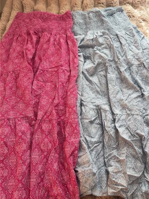 Två långa kjolar med mönster - Säljer två långa kjolar med smock i midjan. Ena kjolen är rosa med vitt paisley-liknande mönster och den andra är ljusblå med liknande mönster. Båda har en luftig och flowy passform, perfekta för varma dagar. 400 för båda