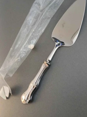 Silverfärgad tårtspade med mönstrat handtag - Elegant tårtspade i silverfärgat metall med ett dekorativt, mönstrat handtag och blank yta. Perfekt för att servera tårta eller paj. Handtaget har fina detaljer och bladet är trekantigt med en lätt tandad kant