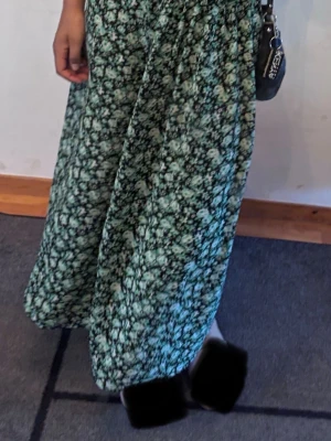 Grön blommig långkjol - Jättefin blommig lång kjol med en slits på sidan. Den är luftig och har resår vid midjan vilket gör den lite mer justerbar/ stretchig. Har används men inga tydliga skavanker.