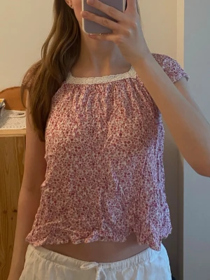 Rosa blommig topp med spets - Söt somrig blommig blus i rosa och vit. Toppen har korta ärmar, spetsdetalj i kragen och är perfekt för sommarens varma dagar ☀️Köpt för drygt ett år sen här på plick för ungefär 80 kr. Säljer då jag känner att den börjar bli för liten för mig. Har använt ett fåtal gånger så toppen är i gott skick 💕storlek 152, men passar xs 💗