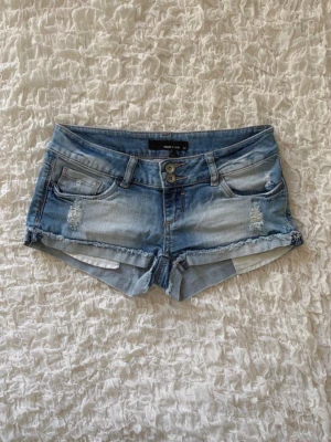 Superfina lågmidjade jeansshorts - Superfina ljusblå denimshorts från Tally Weijl i storlek 34 (XS). Modellen är kort med en snygg dubbelknäppning fram, slitna detaljer både fram och bak samt råa, fransiga kanter nertill. De är i mycket gott skick och perfekta för sommaren! Skickas snabbt, hör av dig vid frågor.💕💕  Midjemåttet är ungefär 35 cm (alla mått finns i bilderna).