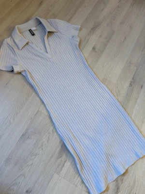 Ribbad ljusbeige klänning  - Supersnygg ribbad klänning från h&m i ljusbeige med krage och v-ringning. Klänningen är kortärmad och har en kroppsnära passform som framhäver siluetten. Perfekt för dig som gillar en stilren och trendig look.