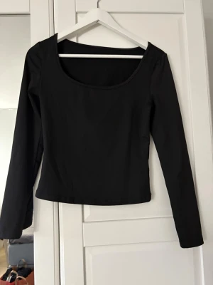 Svart långärmad topp med rund hals - En enkel och stilren svart långärmad topp med rundad urringning. Toppen har en normal passform och är perfekt att matcha med både jeans och kjol. Tillverkad i mjukt material som känns skönt mot huden.